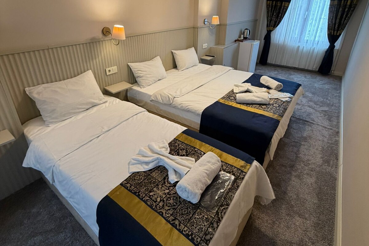 A hotel room with two beds, a ceiling light fixture, and a window with curtains.