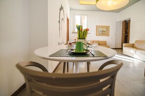 A dining area with a round table, chairs, a green mug, and a vase with flowers. - B&B Arco dei Pinto (Salerno)