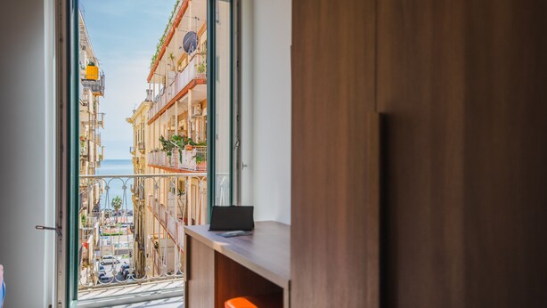 Un balcón con vista a una calle costera, muebles de madera y una puerta.
