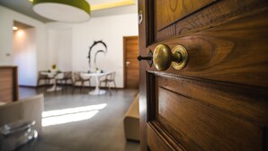 Una puerta de madera con manijas de latón, un comedor con sillas y una mesa, y una lámpara de techo moderna.