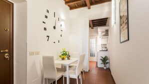 A dining area with a white table and chairs, a wall clock, and a potted plant. - Serpenti Apartment (Roma)