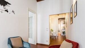 A modern living room with a blue and red armchair, a white door, and a view into a dining area. - Serpenti Apartment (Roma)