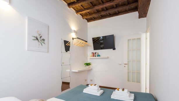 A bedroom with a bed, a mounted TV, a wall-mounted shelf with toiletries, and a door with frosted glass panels. - Serpenti Apartment (Roma)
