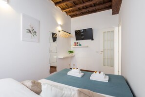 A bedroom with a bed, a mounted TV, a wall-mounted shelf with toiletries, and a door with frosted glass panels. - Serpenti Apartment (Roma)