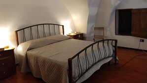 Ein Schlafzimmer mit einem Bett, Nachttischen, einem Holzstuhl und einem Fenster mit einem Holzklappladen.