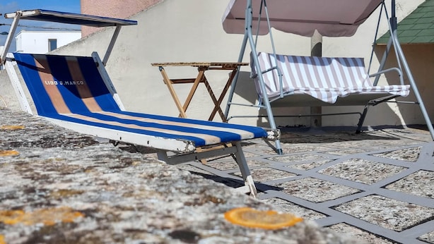 Zwei Liegestühle mit Sonnenschirmen, ein kleiner Tisch und eine geflieste Terrassenfläche.