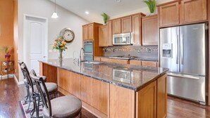 A modern kitchen with wooden cabinets, stainless steel appliances, a central island, and bar stools. - 4 Bed/3 Bath, Sleeps 12! 20 min DIA, Pets-Large yard; Great for Families! (Commerce City)