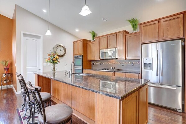 A modern kitchen with wooden cabinets, stainless steel appliances, a central island, and bar stools.