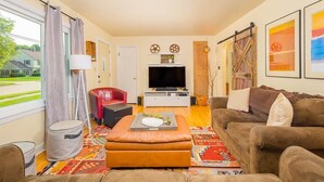 Ein Wohnzimmer mit einer Couch, einem Hocker und einem Fernseher-Lowboard.
