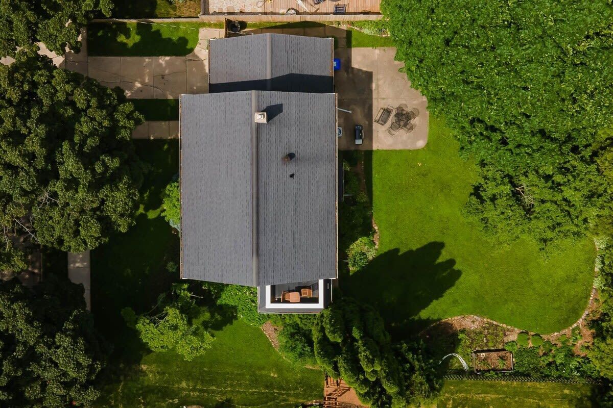 An aerial view of a modern house with a flat roof, surrounded by lush green lawns and trees.