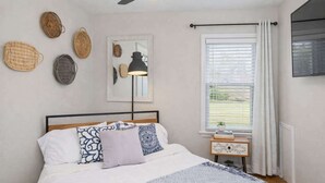 A bedroom with a bed, bedside table, lamp, and window with curtains.