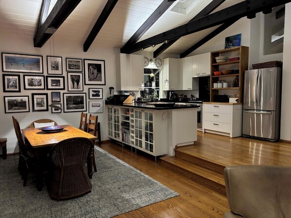 Una cucina moderna con mobili bianchi, un frigorifero in acciaio inossidabile e un'area pranzo con tavolo e sedie in legno.