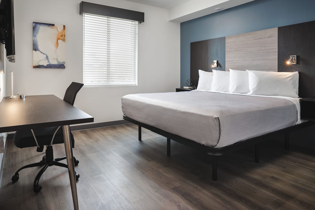 Moderni hotellihuone, jossa on suuri sänky, työpöytä ja ikkuna, jossa on sälekaihtimet.