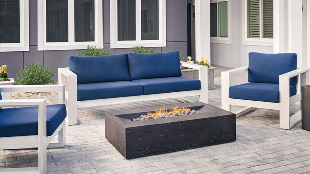 Een modern terras met een blauwe bank, witte fauteuils en een zwarte vuurkorf.
