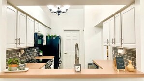A kitchen with white cabinets, a black refrigerator, a sink, and a countertop with a clock and a sign that reads "Welcome Make yourself at Home".