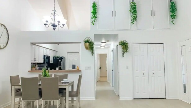 A modern kitchen with white cabinets, a dining area with a table and chairs, and a hallway with white doors and green plants.
