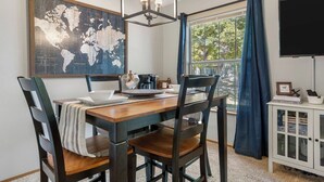 Un comedor con una mesa de madera, sillas, un mapa mundial, una cafetera y un televisor sobre un mueble.
