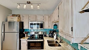 A kitchen with a stainless steel refrigerator, a microwave, an oven, and a coffee maker. There are wooden cabinets and a tiled backsplash. - End Unit Condo | Beach Views | Pool & Hot Tub (Destin)