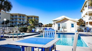 A pool area with lounge chairs and a small building, surrounded by multi-story buildings. - End Unit Condo | Beach Views | Pool & Hot Tub (Destin)
