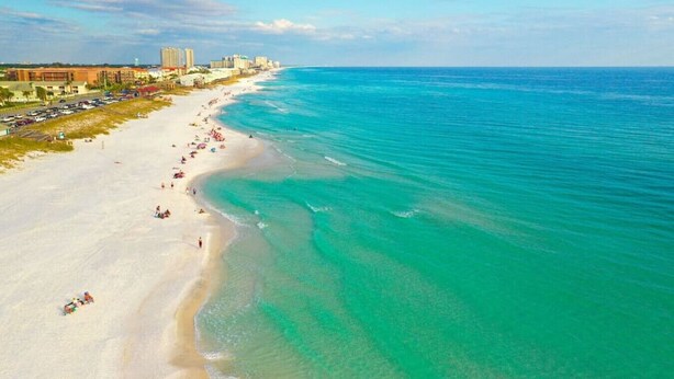 A coastal beach with a long stretch of sandy shore, a clear blue sea, and buildings along the coastline. - End Unit Condo | Beach Views | Pool & Hot Tub (Destin)