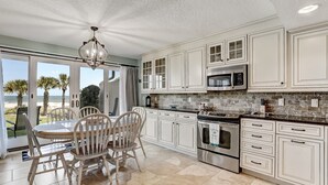 A kitchen with white cabinets, a stainless steel oven, and a view of the beach.