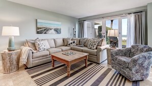 A living room with a sofa, a patterned armchair, a coffee table, and a side table with a lamp.