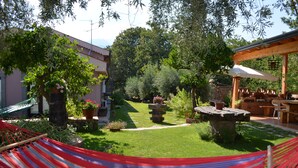 Un jardín con una hamaca, una mesa de piedra y una pérgola con una sombrilla.