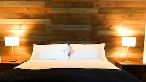 Un lit avec une literie blanche et deux lampes de chevet, placé devant un mur en bois.