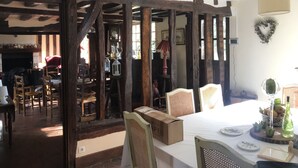 A rustic room with exposed wooden beams, a fireplace, and a dining area with a table set for two. - Normandy vacation home with swimming pool 12km from Verneuil sur avre (Mesnils sur Iton)