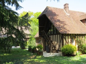 A traditional timber-framed house with a steeply pitched roof, a visible staircase, and a well-maintained garden with various plants and a pathway. - Normandy Vacation Home with Pool, 12 km from Verneuil-sur-Avre (Mesnils sur Iton)