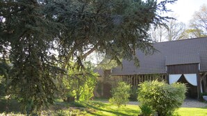 A rustic building with a tiled roof and wooden walls, surrounded by a well-maintained garden with various shrubs and a lawn. - Normandy vacation home with swimming pool 12km from Verneuil sur avre (Mesnils sur Iton)