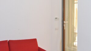 Een rode bank in een kamer met een witte muur en een glazen deur die uitkomt op een zonnig buitengebied.