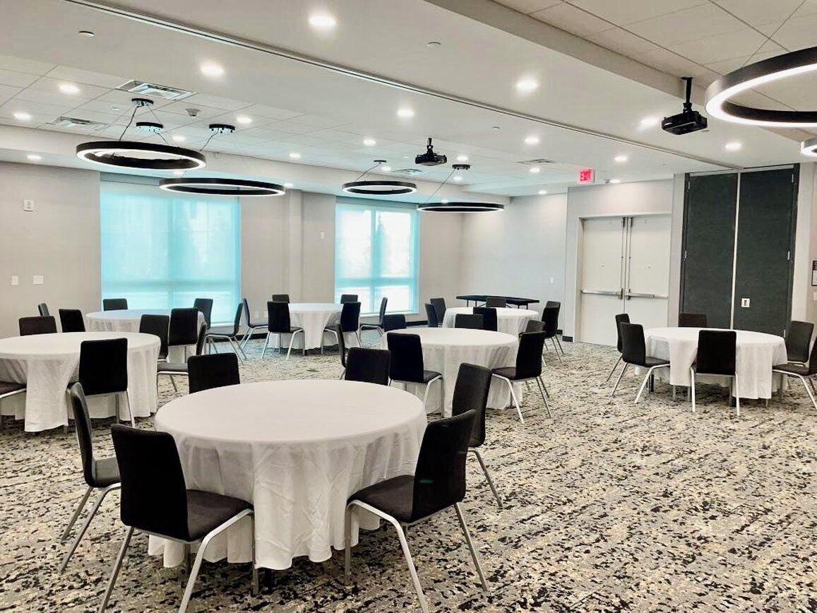 A conference room with round tables, black chairs, and white tablecloths.