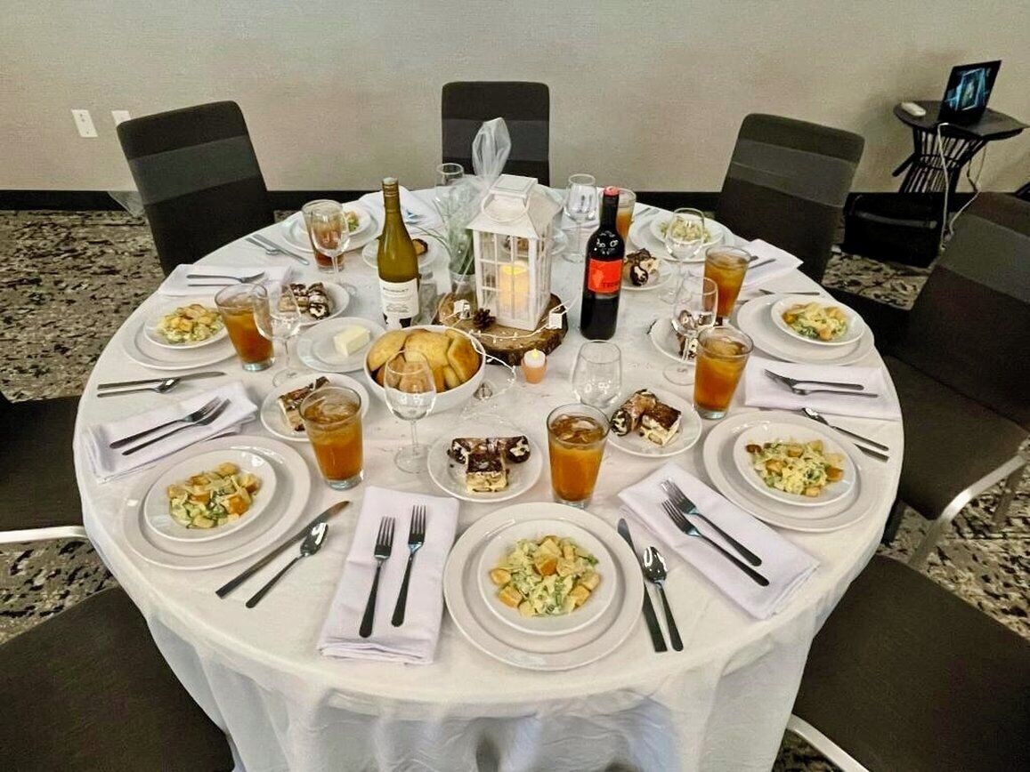 A round dining table set for a meal with various dishes, glasses, and a bottle of wine.