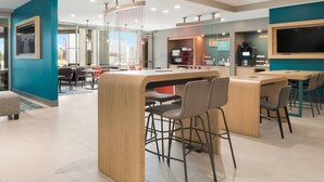 Un área de bar moderna con mostradores de madera y taburetes, una pantalla grande y un espacio de estar con mesas y sillas.