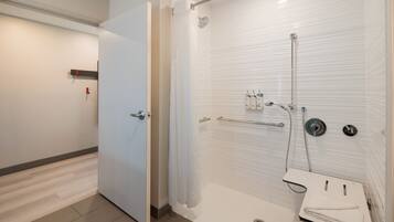 Une salle de bain moderne avec une douche à l’italienne, un lavabo blanc avec une serviette, et une porte donnant sur une autre pièce.
