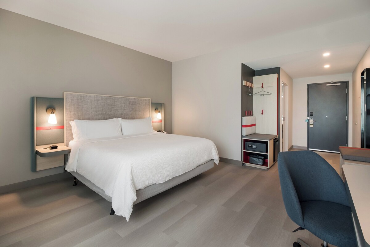 Une chambre d’hôtel moderne, dotée d’un grand lit, de tables de chevet, d’un bureau et d’une chaise.