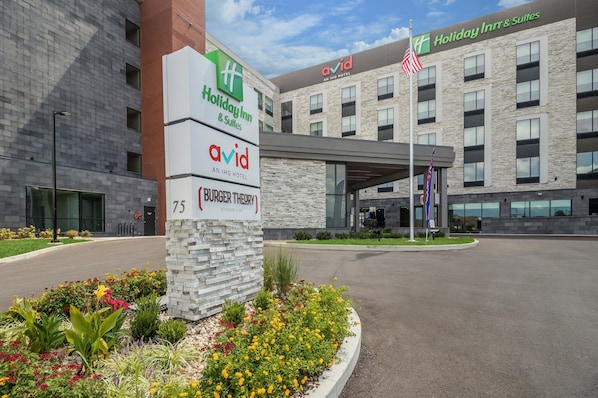 A Holiday Inn & Suites with a Burger Theory restaurant sign, a flag, and a landscaped entrance.