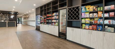 A modern retail area with shelves stocked with snacks and beverages, wooden flooring, and a clean, well-lit environment.