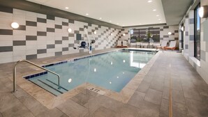 Una piscina interior con pared de azulejos, una silla de socorrista y una tumbona.