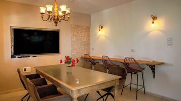 A dining area with a large table, chairs, a chandelier, wall-mounted lights, and a TV.