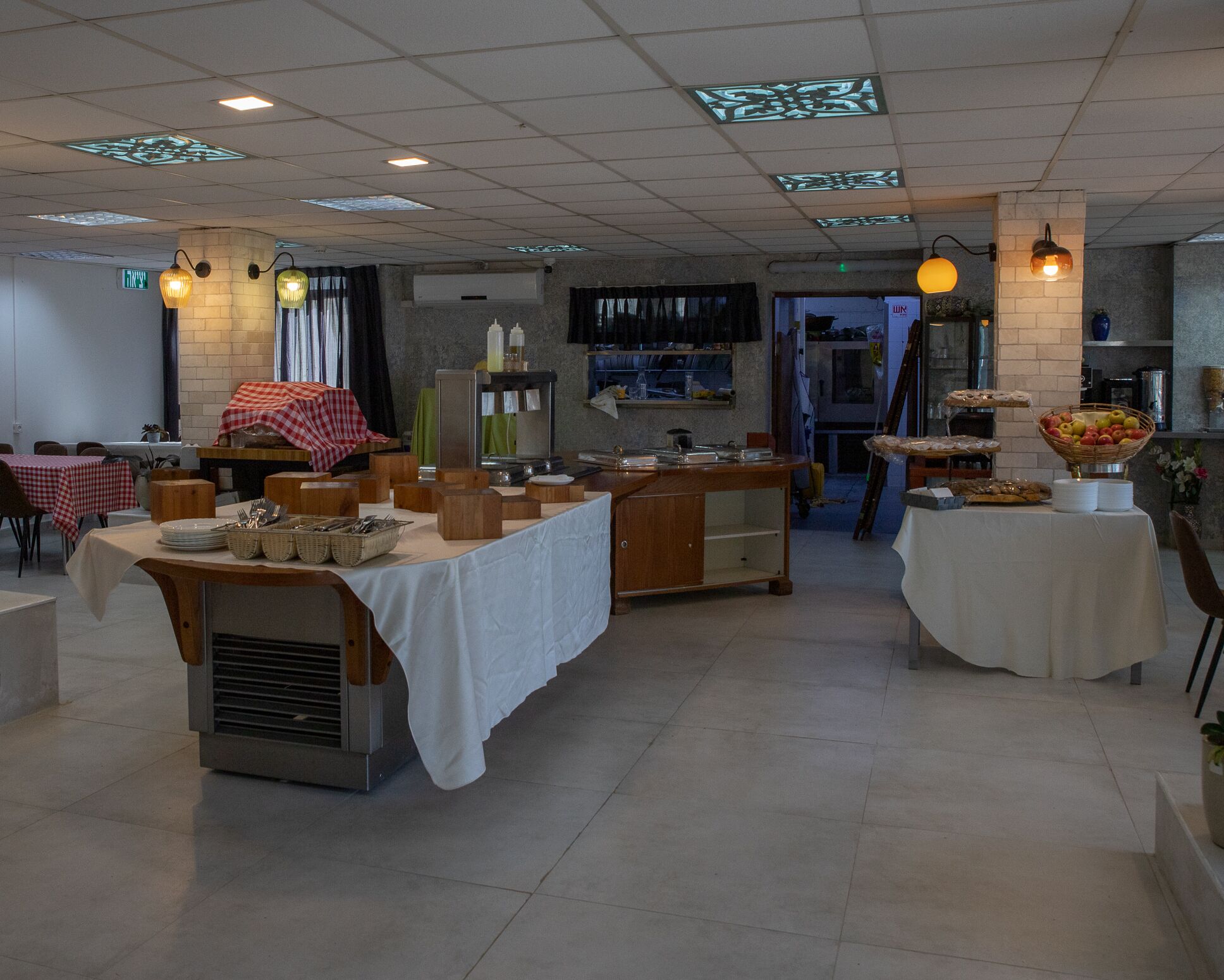 A dining area with multiple tables, some covered with white tablecloths, and a variety of food items displayed on stands.