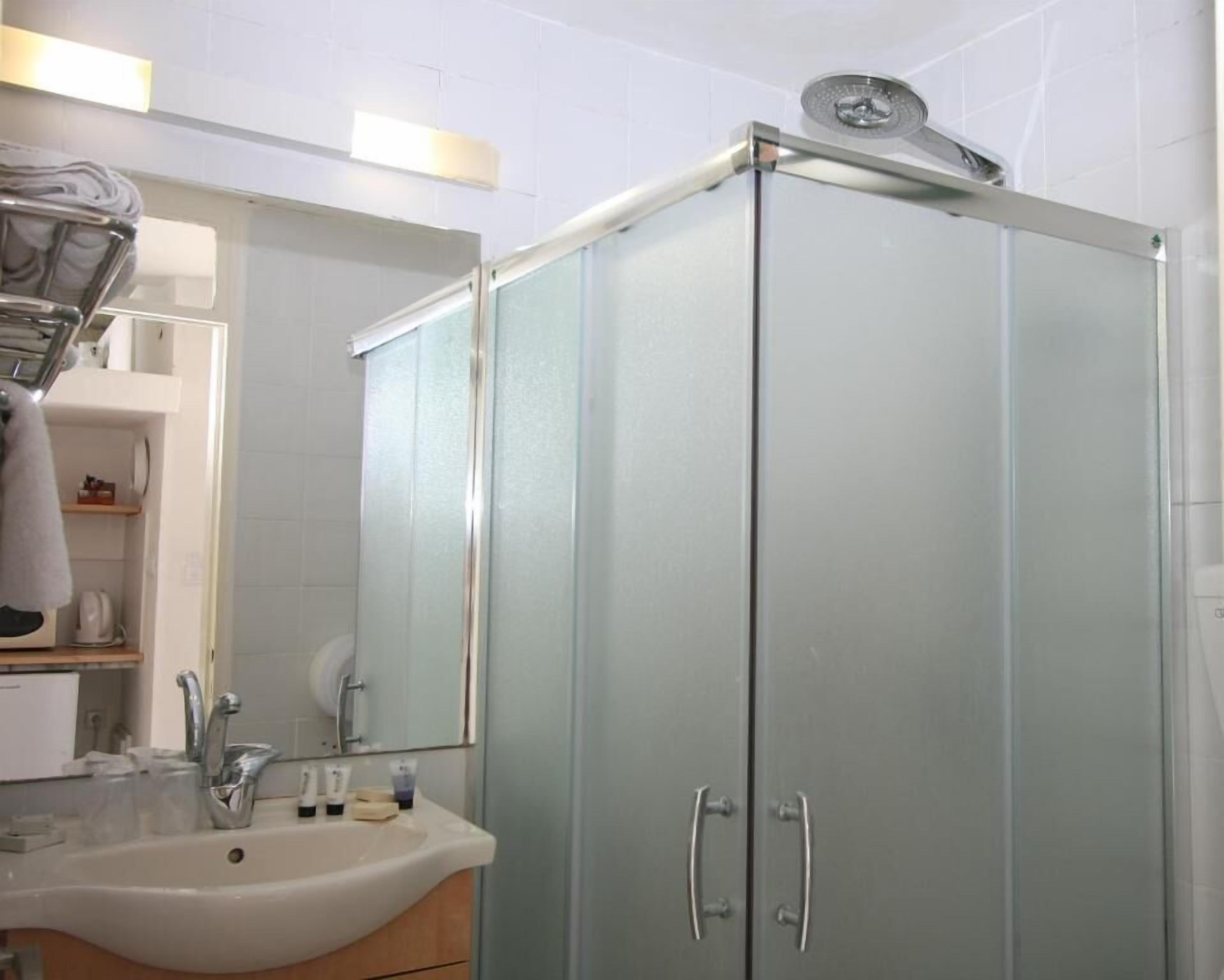 Un baño con ducha de vidrio, un lavamanos con artículos de aseo y un espejo.