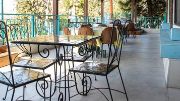 Un patio al aire libre con mesas y sillas de metal, piso de baldosas y techo de madera.