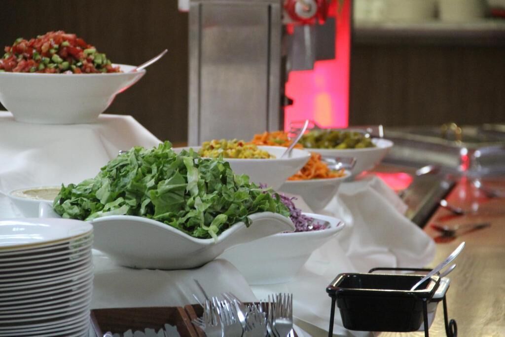 A buffet table with various dishes, including salads and a bowl of red sauce.