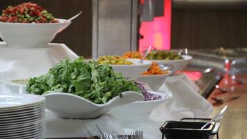 A buffet table with various dishes, including salads and a bowl of red sauce.