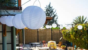 An outdoor patio with round tables and chairs, hanging paper lanterns, and a wooden fence in the background.