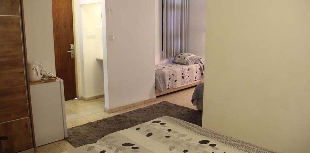 A bedroom with a bed, a small table, and a door leading to another room.