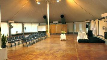 A large hall with rows of chairs, a stage with a table, and a ceiling with lights.