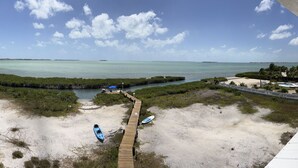Una playa con un paseo de madera que lleva a un muelle, un kayak y una tabla de surf.